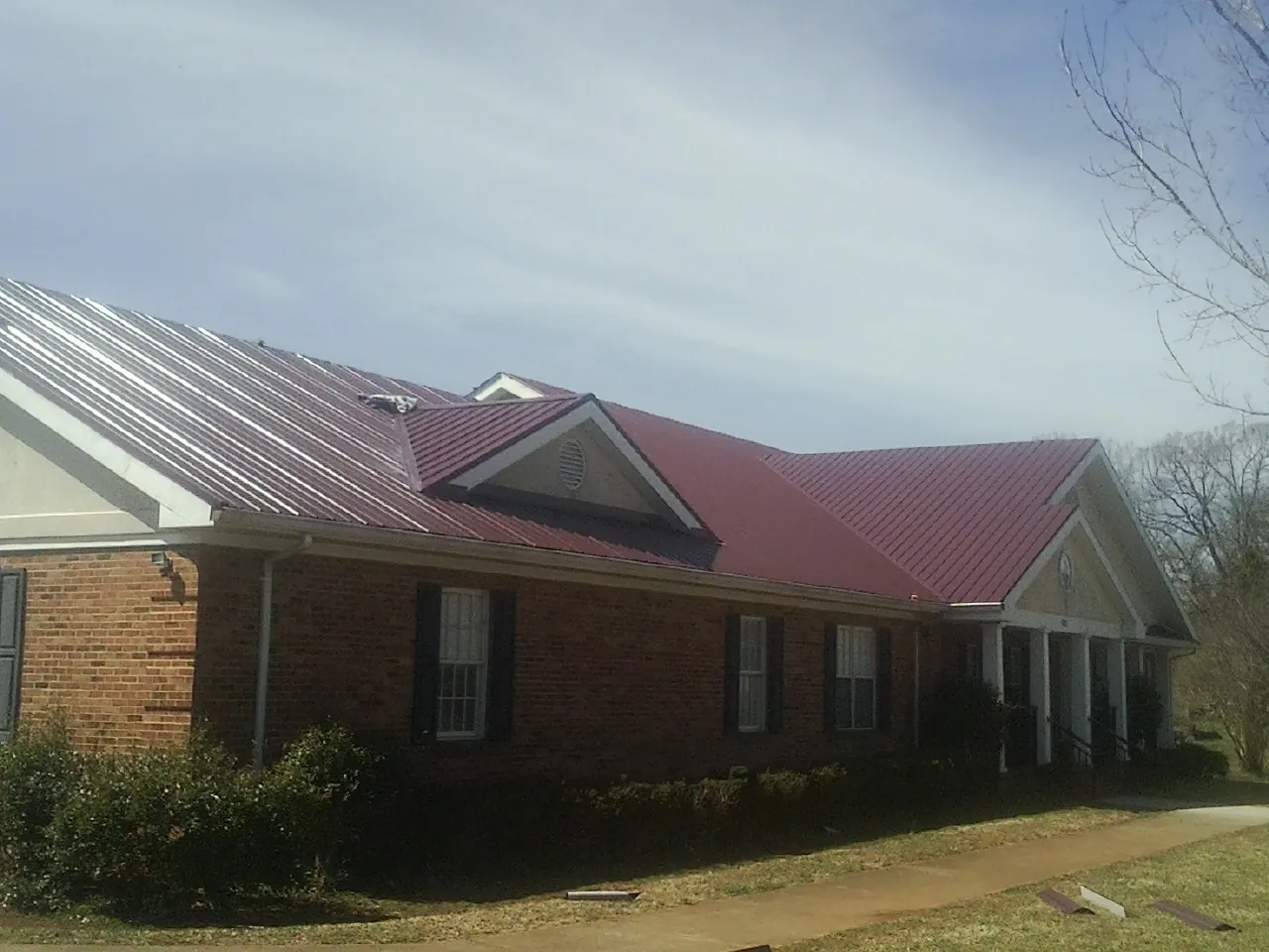 Red metal roof with gabled entries on a long brick building, from a Hail Damage Roof Repair job in Factoryville