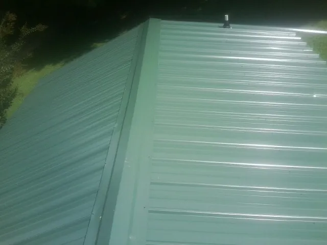 New green metal panels meeting at the ridge of a roof — Flat Roof Repair work by our crew in Factoryville
