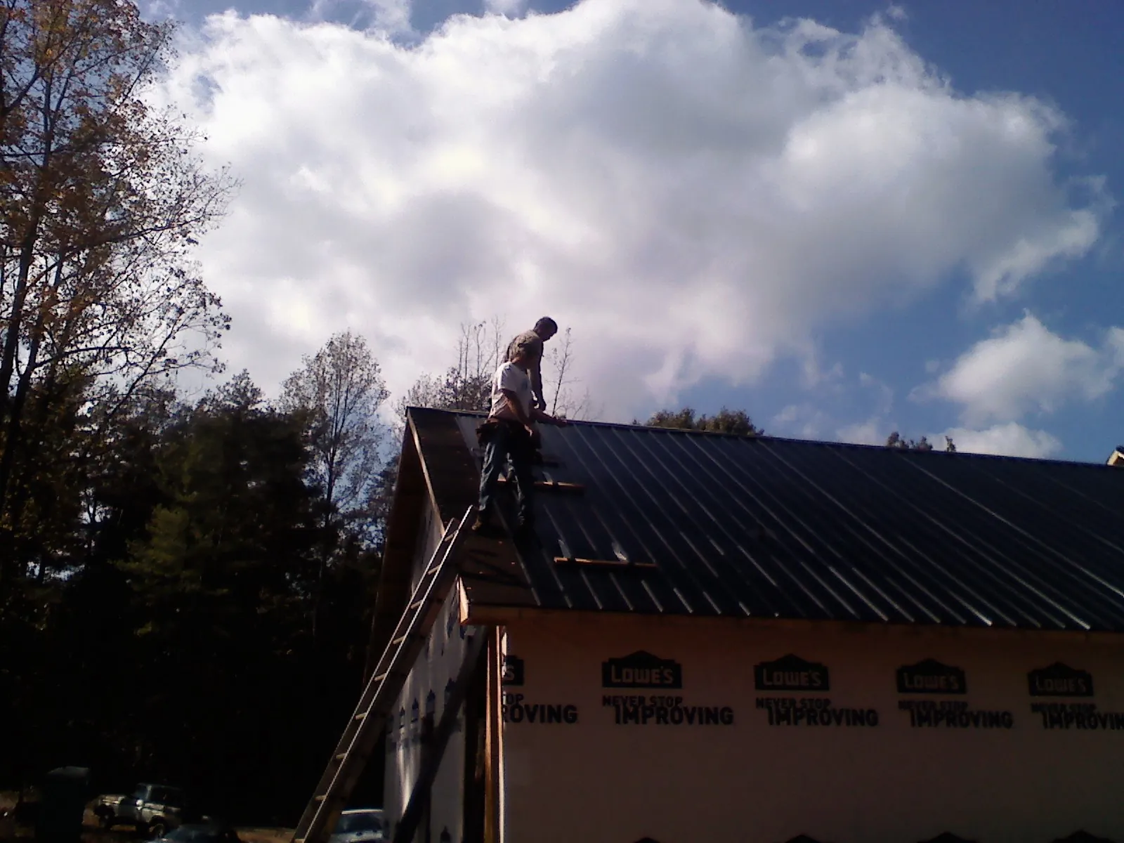 Roofer fastening dark metal panels high against a cloudy sky, from a Roof Inspection job in Factoryville