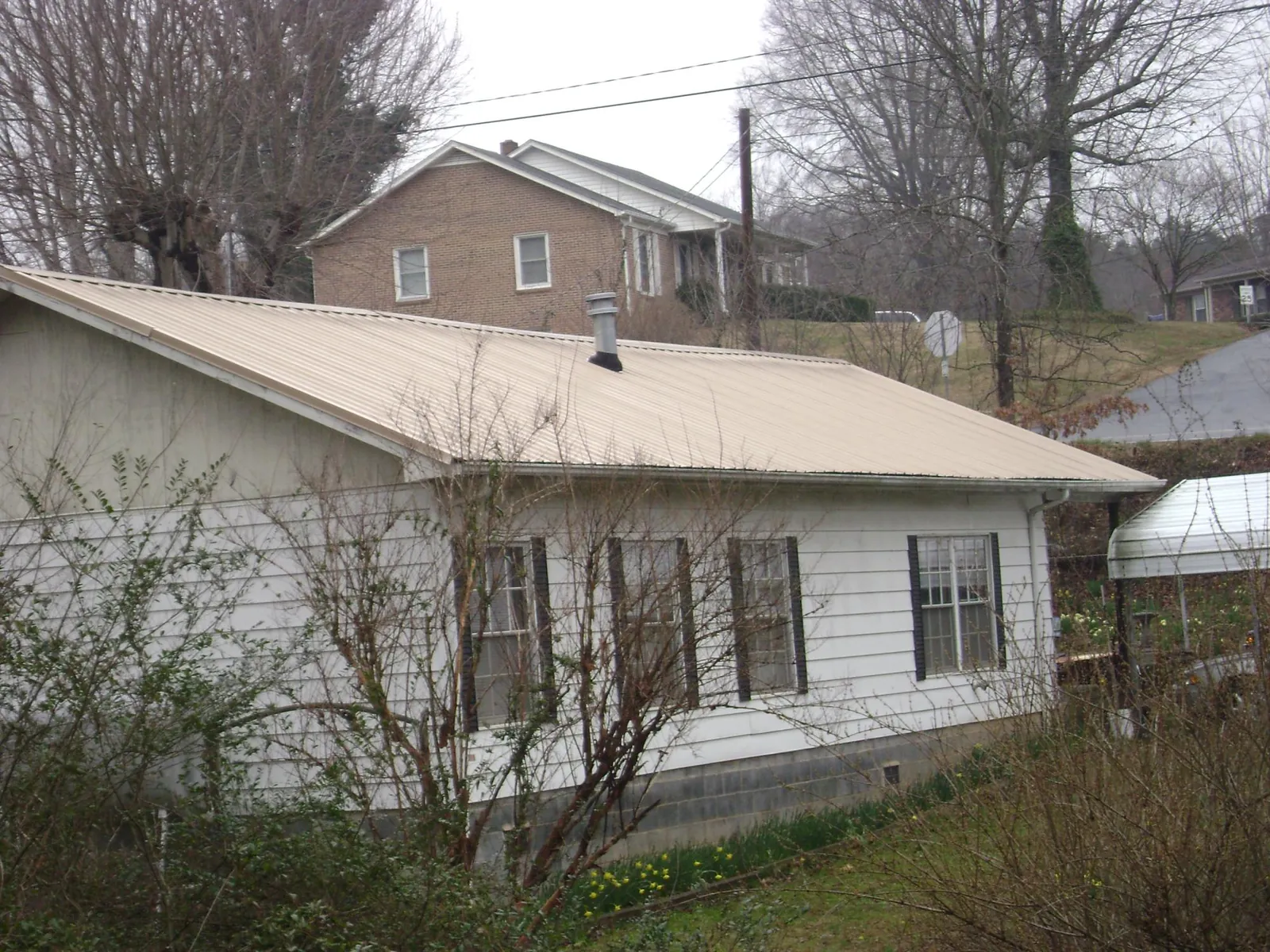 Tan metal roof on a white sided house set into a hillside — Commercial Roofing by Roofing Brothers in Factoryville